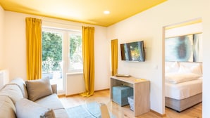 A modern room with a sofa, a small desk, a bed, and a TV on the wall. - Boutiquehotel Caravella (Velden am Wörther See)