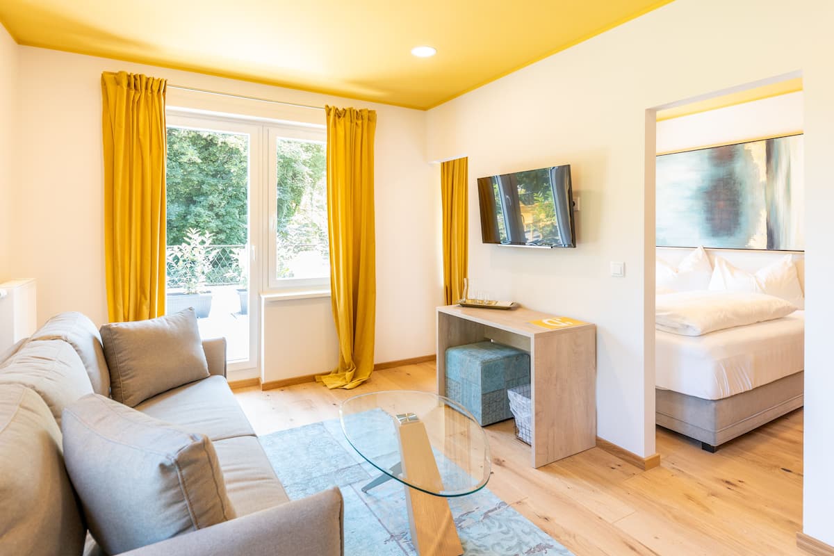 Une chambre moderne avec un canapé, un petit bureau, un lit et un téléviseur fixé au mur.