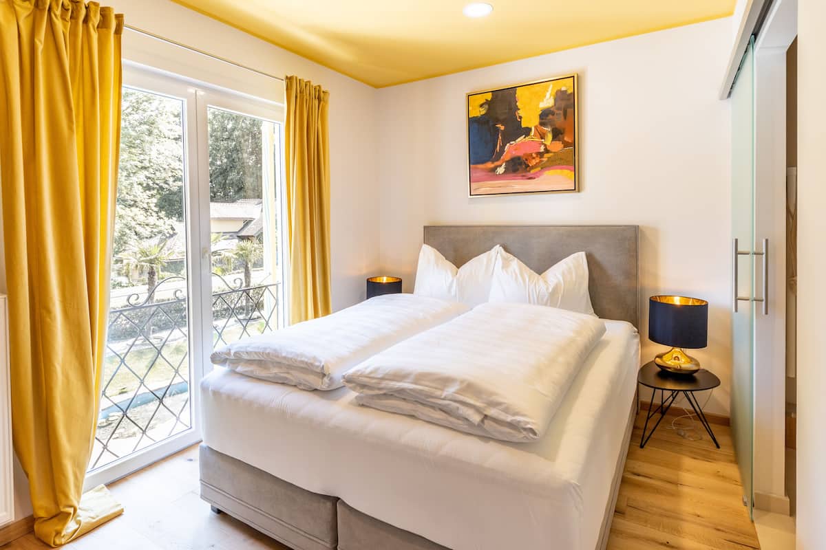 Un lit double avec du linge de lit blanc, une table de chevet avec une lampe et un tableau au mur.