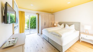 A modern bedroom with a large bed, a desk, and a TV mounted on the wall. - Boutiquehotel Caravella (Velden am Wörther See)