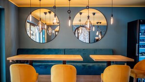 A restaurant with a wooden table and yellow chairs, a blue cushioned bench, and two round mirrors on the wall. - Boutiquehotel Caravella (Velden am Wörther See)
