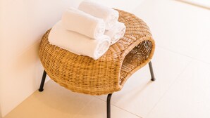 A bathroom with a white sink, a mirror, and a wicker stool with towels. - Boutiquehotel Caravella (Velden am Wörther See)