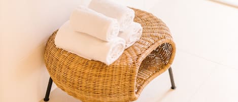 Un baño con lavamanos blanco, un espejo y un taburete de mimbre con toallas.