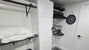 A compact room with a bed, a white wardrobe, a drying rack, and a small storage area with bins. - Spectacular Modern Luxury! (Tillamook)