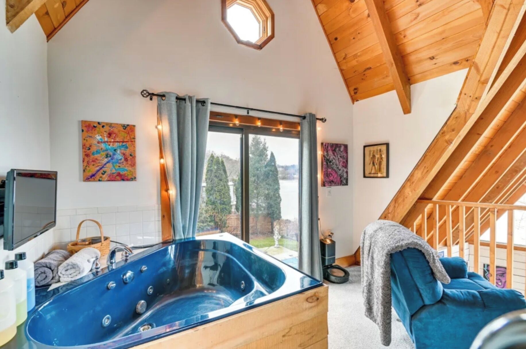 A modern bathroom with a glass bathtub, a large window with curtains, and a wooden ceiling.