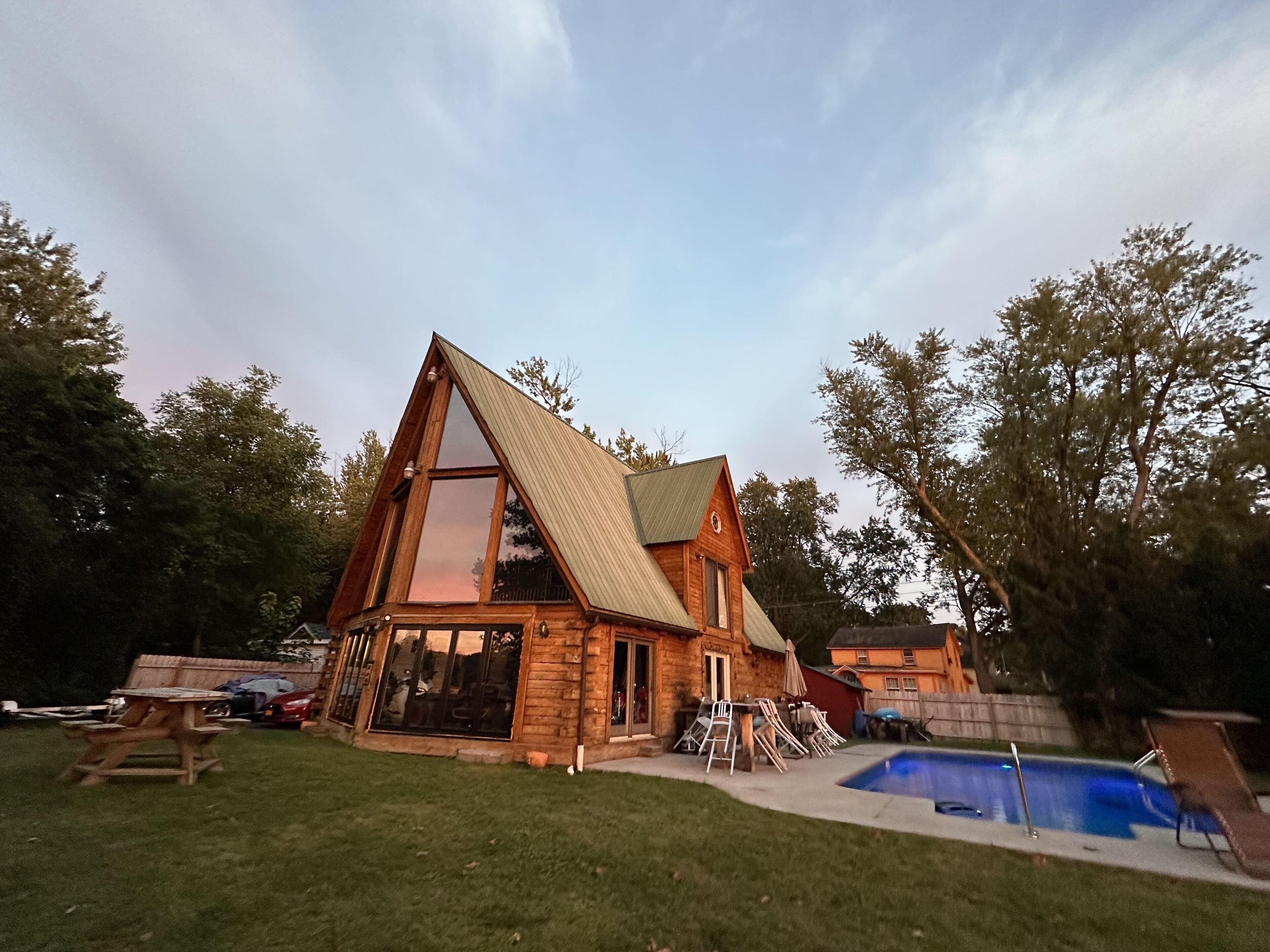 Una casa de madera con techo triangular, piscina y césped.