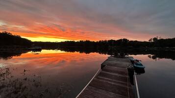 Un muelle de madera que se adentra en aguas tranquilas con un atardecer de fondo.