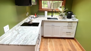 A compact kitchen with a built-in stove, white cabinets, a window with a view of greenery, and a skylight. - Private garden cottage located in the heart of downtown.  (Leesburg)