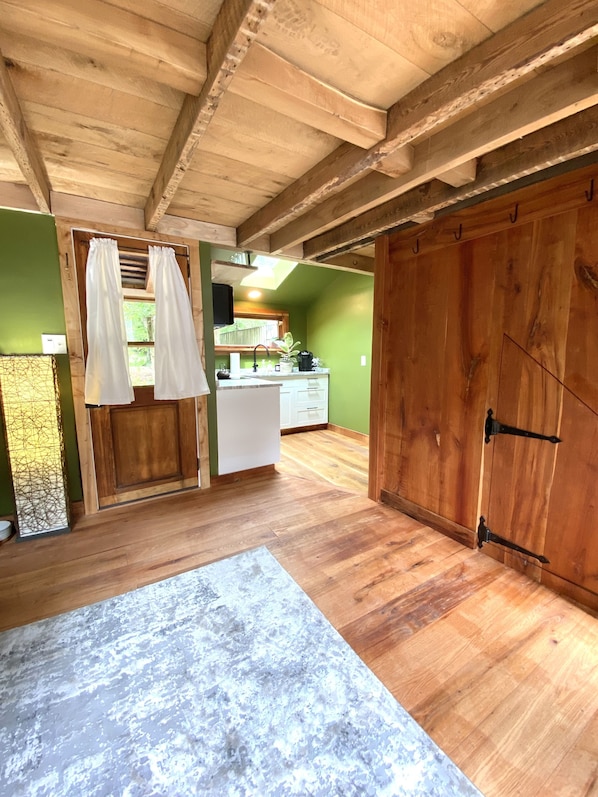 A rustic kitchen with wooden beams, a white countertop, and a large wooden door.
