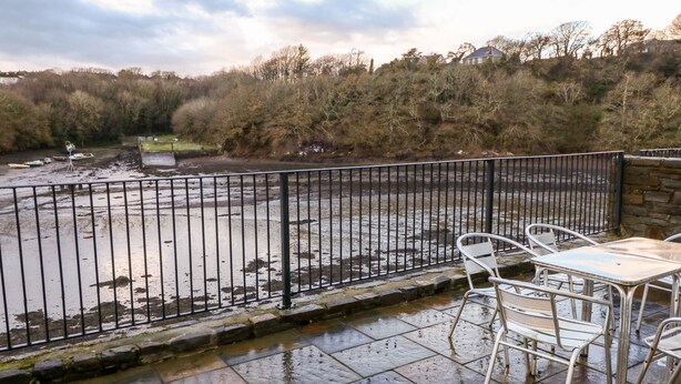 A riverside patio with a stone table and chairs, a metal fence, and a view of a river and trees. - Egret (Milford Haven)