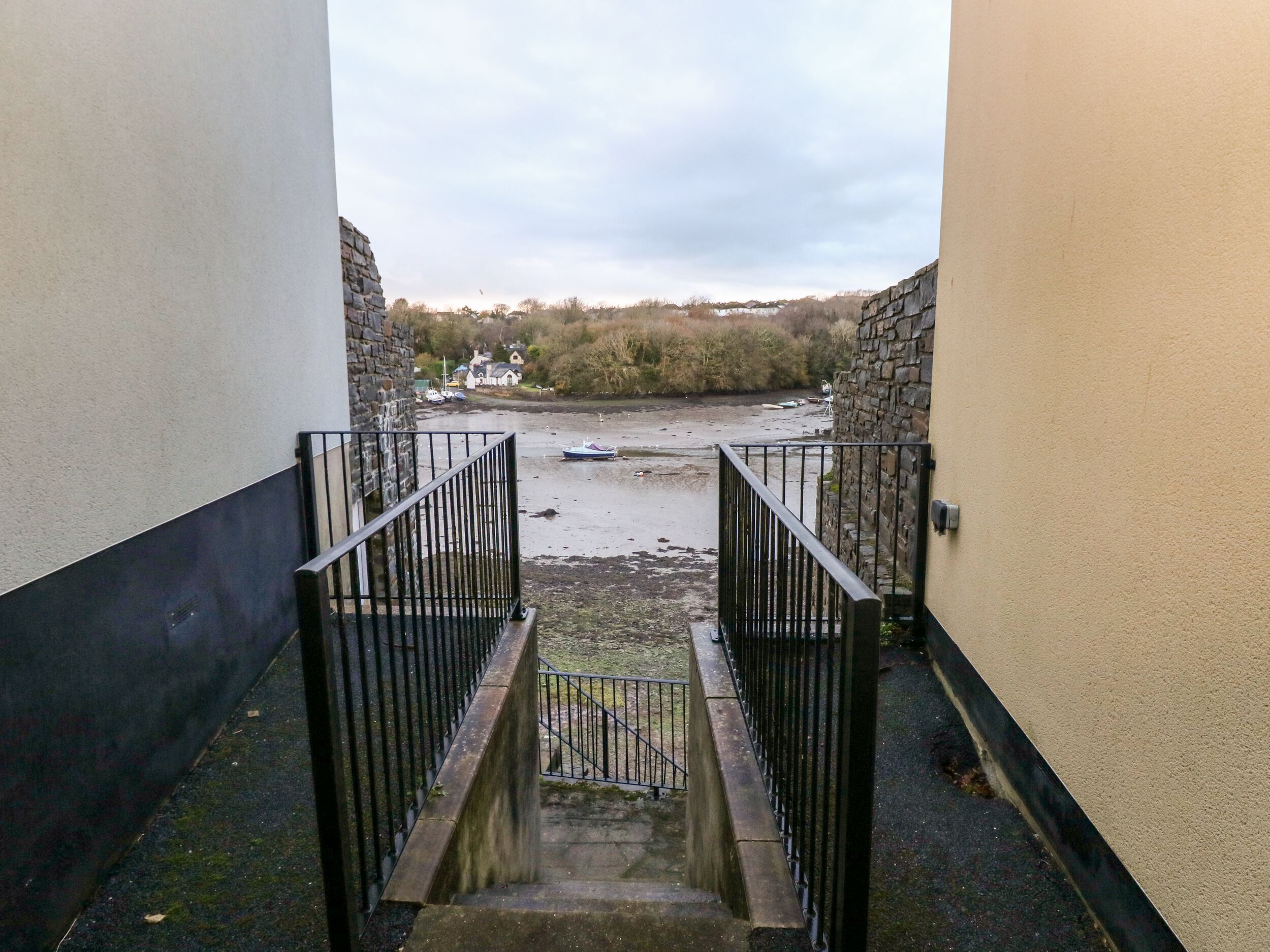 A narrow stairway leading to a waterfront area with stone walls and a view of boats on the water.