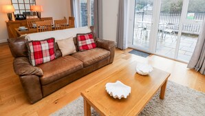 A cozy living room with a brown leather sofa, two plaid cushions, a wooden coffee table, and a dining area with a wooden table and chairs. - Egret (Milford Haven)