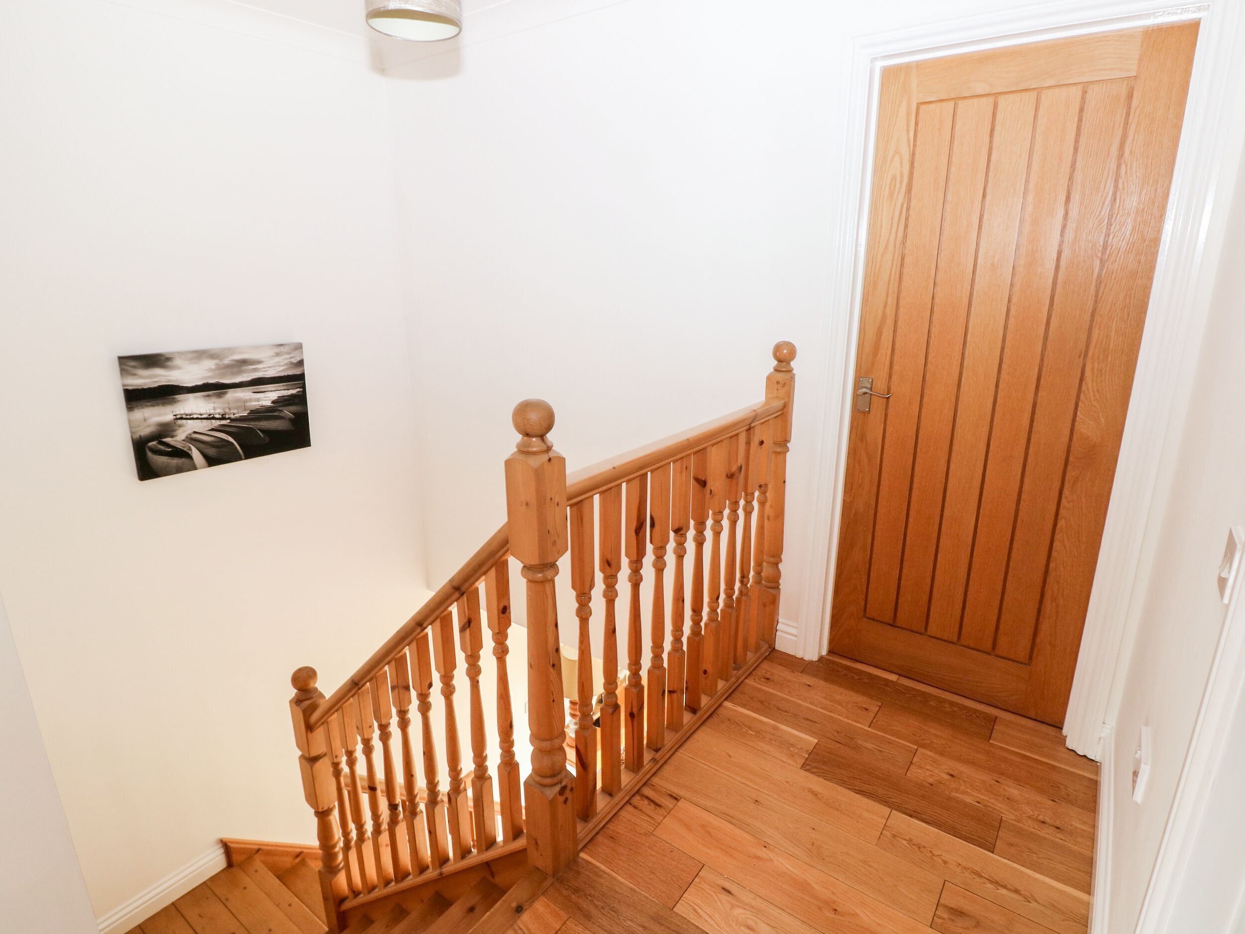 Eine Holztreppe mit Handlauf, eine Holztür und ein gerahmtes Bild an der Wand.