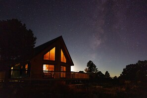 A cabin with large windows, a deck, and a view of the night sky.