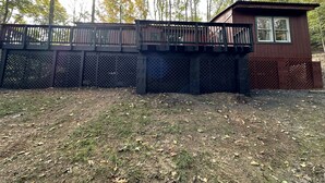 A wooden deck with a lattice fence, a small building with a window, and a grassy area with trees in the background.