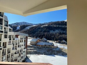 Vista de uma varanda com vista para uma paisagem nevada, com edifícios e uma montanha ao fundo.