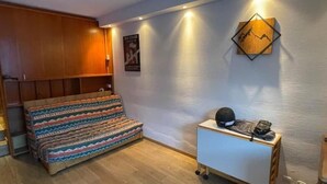 Une chambre avec un lit, une petite table sur laquelle se trouve un casque, et une affiche accrochée au mur.