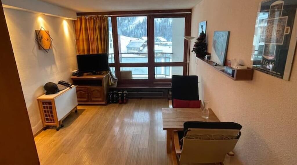 Un salon chaleureux avec un plancher en bois, un téléviseur, une cheminée et une grande fenêtre donnant sur un paysage enneigé.