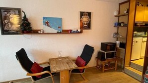Un petit coin repas avec une table en bois et deux chaises, une petite étagère ornée d’objets décoratifs et un four à micro-ondes posé sur un meuble en bois.