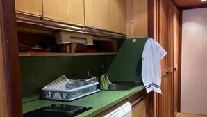 Une cuisine compacte avec des meubles en bois, un plan de travail vert, un petit lave-vaisselle et une serviette accrochée à la porte.
