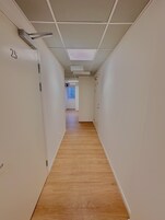 A narrow hallway with wooden flooring and white walls, leading to a door with a number sign.
