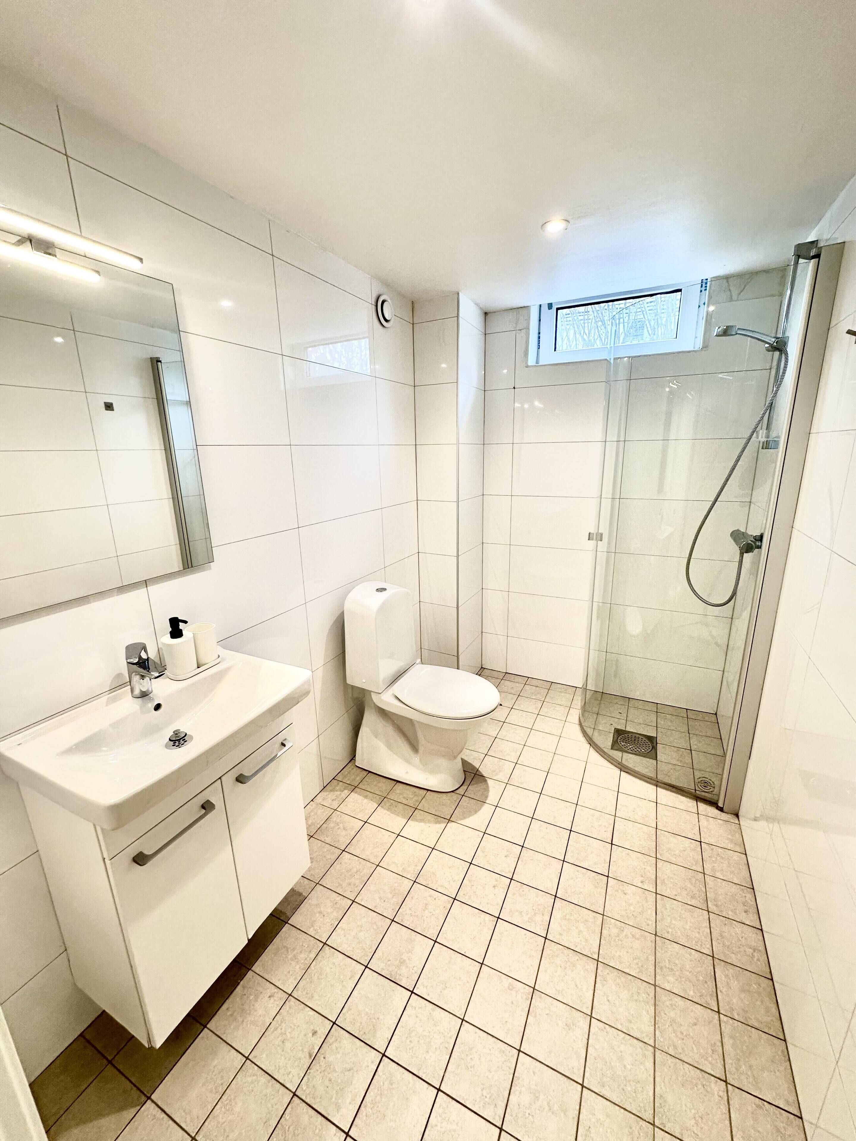 A modern bathroom with a white sink, toilet, and glass-enclosed shower.