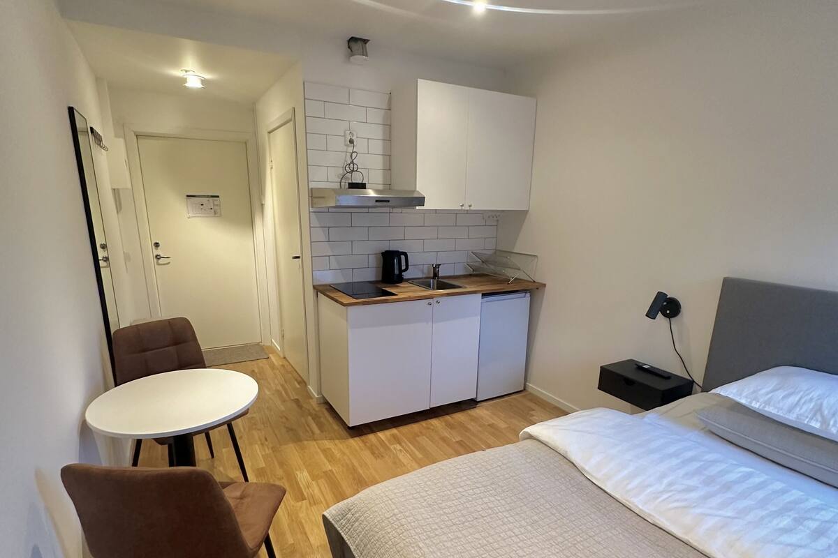 Een compacte hotelkamer met een bed, een kleine kitchenette, een eethoek met tafel en stoelen, en een badkamer in de achtergrond.