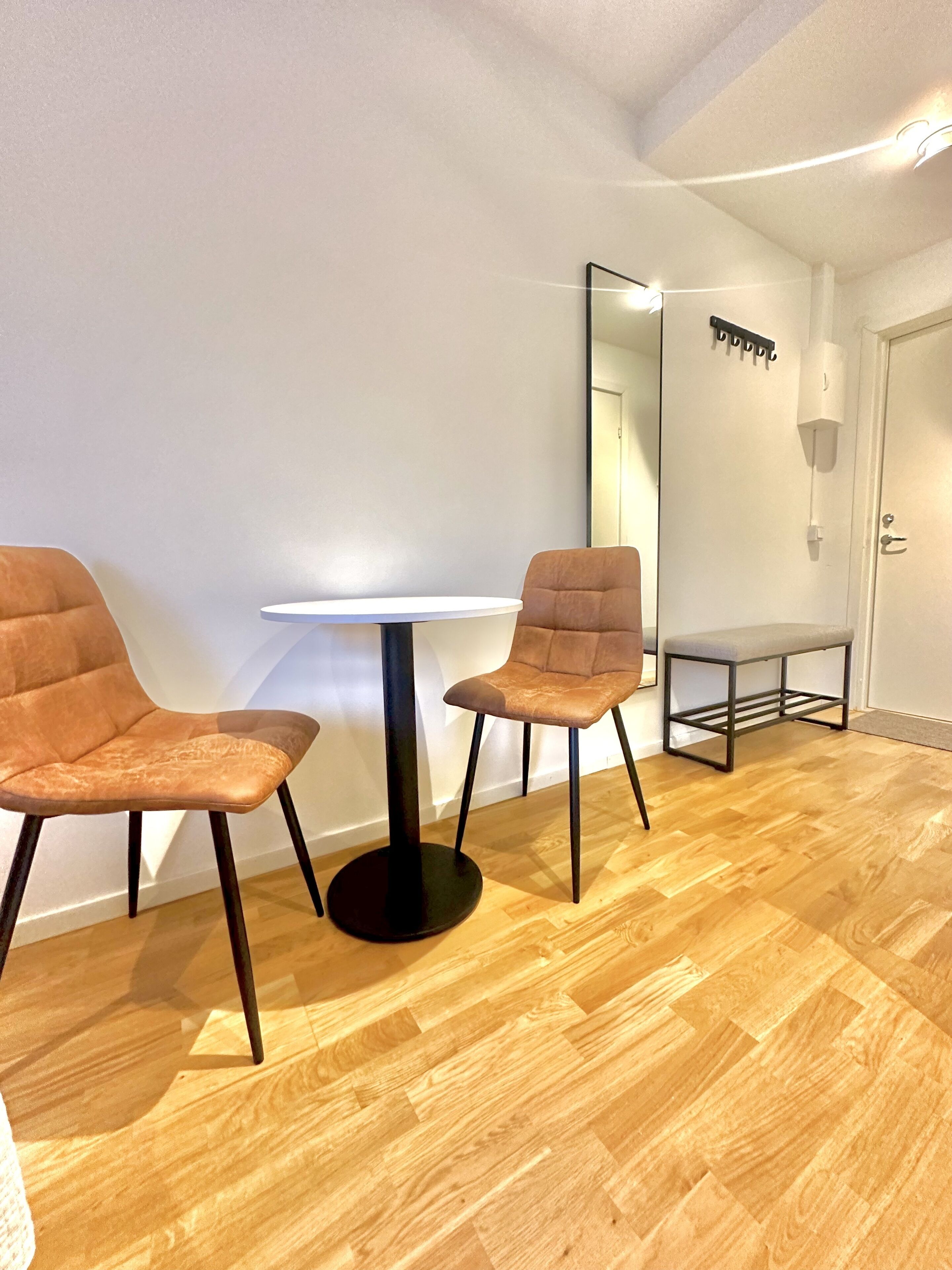 Une pièce avec deux fauteuils marron, une table blanche et un miroir au mur.