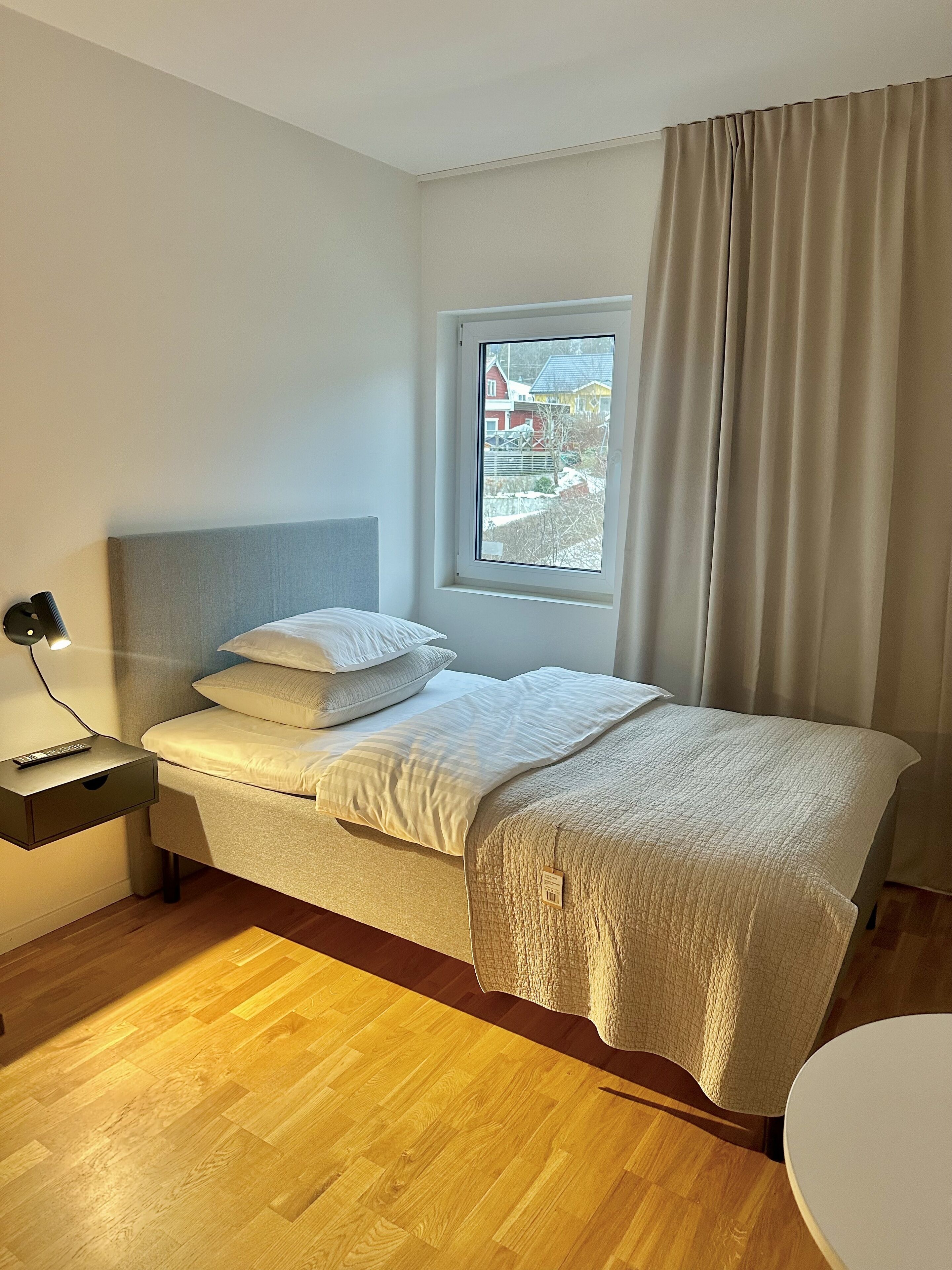 A bedroom with a bed, bedside table, lamp, and a window with curtains.