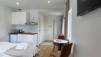 Ett modernt hotellrum med två sängar, ett litet pentry, en matplats med bord och stolar samt en TV som är monterad på väggen.