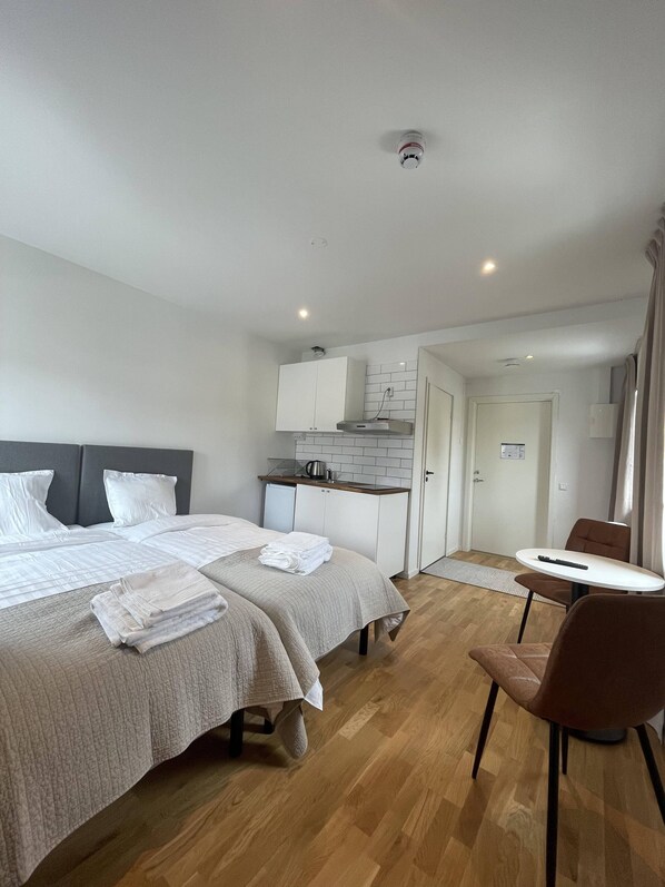 Una habitación de hotel moderna con dos camas, kitchenette, comedor y baño.