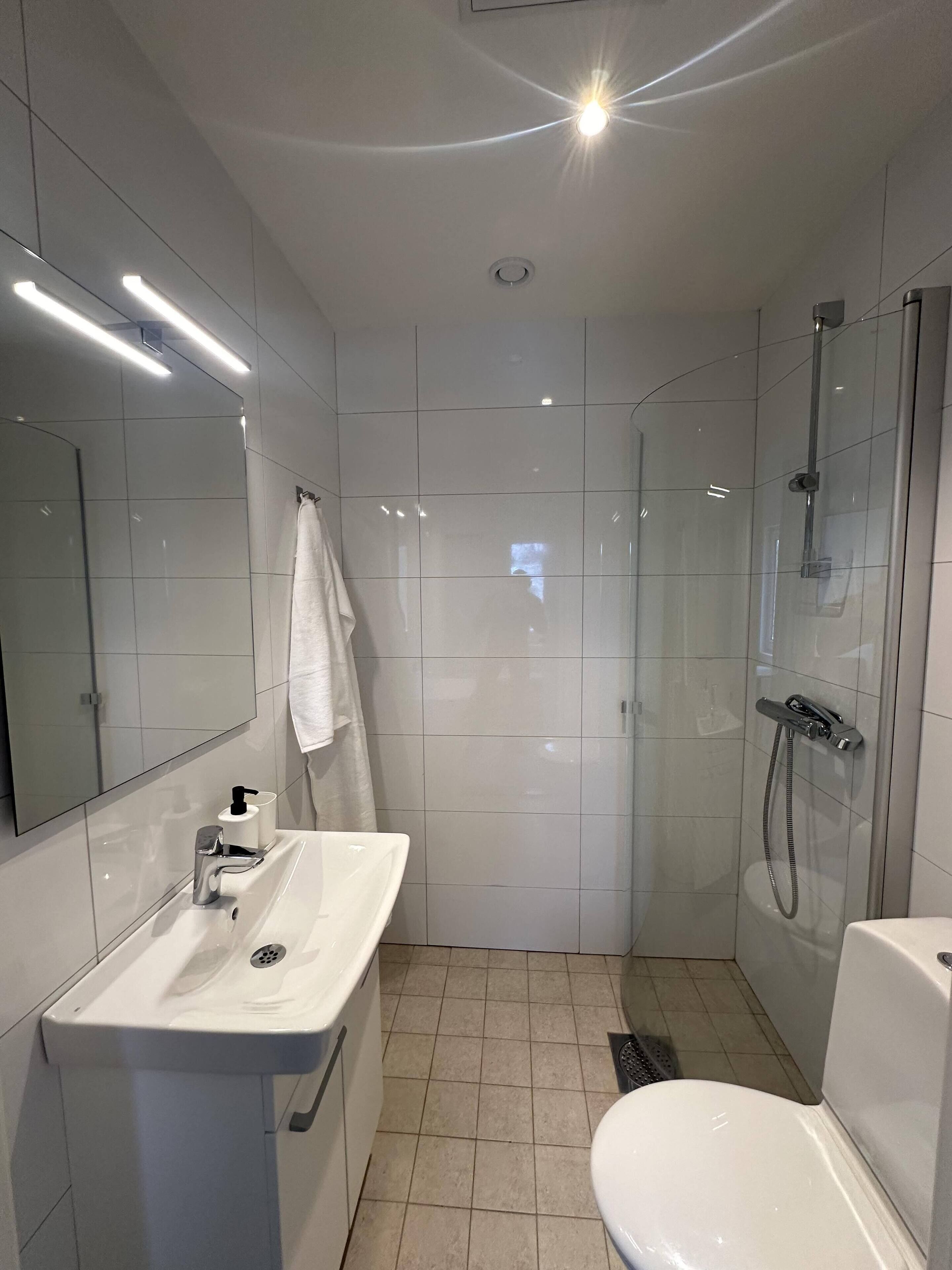 Un baño moderno con lavamanos, espejo y retrete blancos.