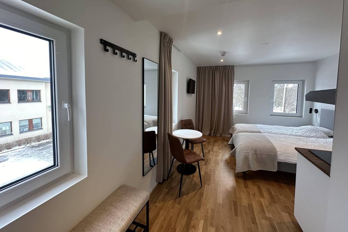 Een hotelkamer met een groot raam, een bed, een nachtkastje, een stoel en een spiegel.