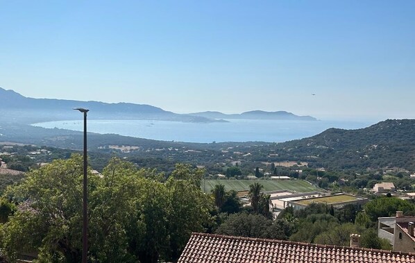 Un paysage côtier offrant une vue dégagée sur la mer, avec des collines douces et un avion aperçu au loin.
