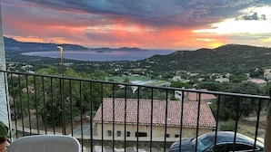 En balkon med udsigt over et kystlandskab i solnedgang.
