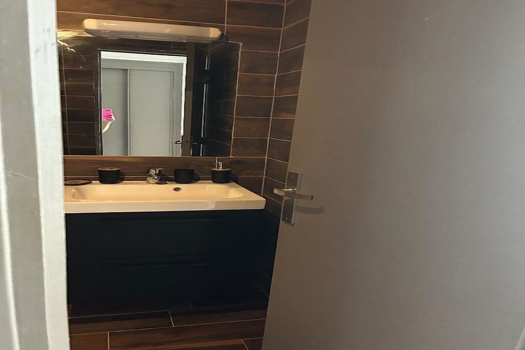 A bathroom with a large sink, dark tiles, and a mirror.