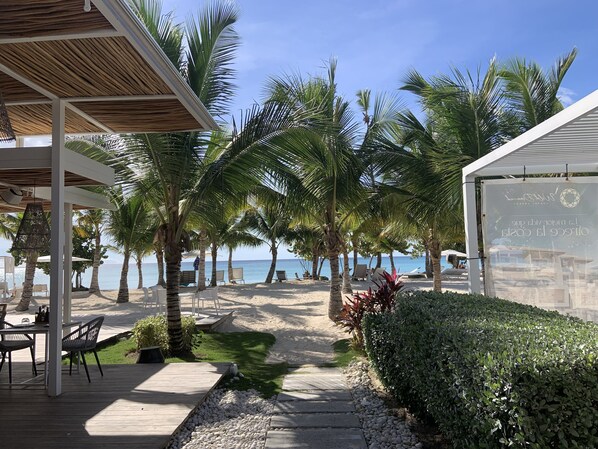 A beachside patio with a wooden deck, lounge chairs, and a view of the ocean.