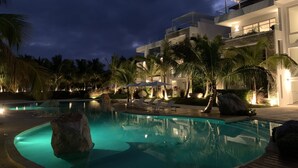 A modern resort with a swimming pool, palm trees, and a well-lit building at night.