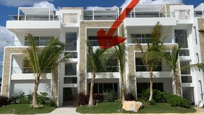 A modern multi-story hotel with balconies, palm trees, and a clear blue sky.
