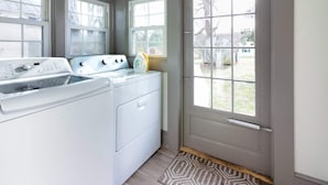 A laundry room with a front-loading washer and dryer, a window, and a door leading outside. - Cozy Country Getaway in the Heart of Upperville  (Upperville)