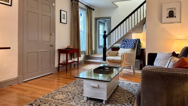 A living room with a glass coffee table, a patterned rug, a sofa, and a chair. A staircase is visible in the background. - Cozy Country Getaway in the Heart of Upperville  (Upperville)