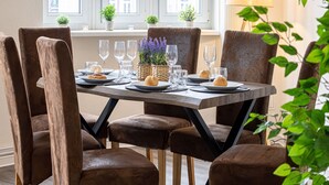 Mesa de comedor dispuesta para seis personas, con sillas tapizadas en marrón, una lámpara y una ventana con vista a edificios.