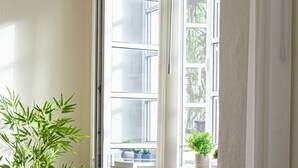 Una habitación con sofá, ventana con vista a follaje y planta en el alféizar.