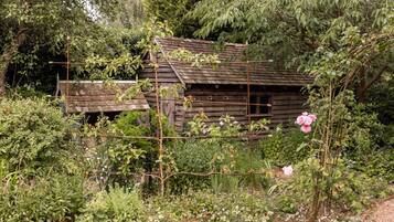 Una cabaña de madera rústica rodeada de follaje denso y plantas en flor.