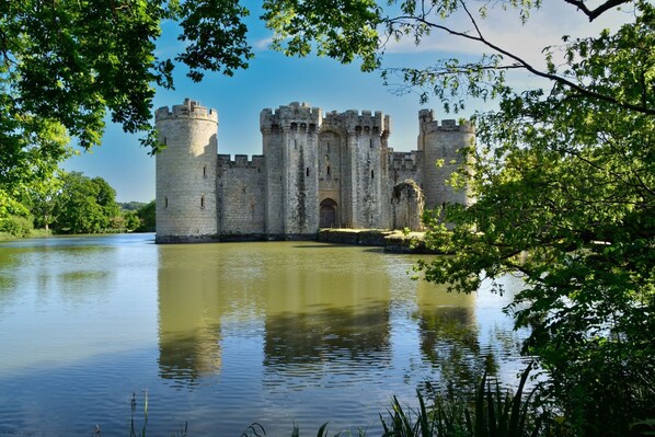 Un castillo histórico con un foso, rodeado de exuberante vegetación y un cielo despejado.