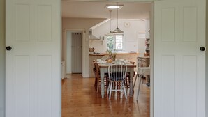 Un área de comedor con una mesa y sillas de madera, una lámpara colgante y vistas a una cocina con armarios y una ventana.