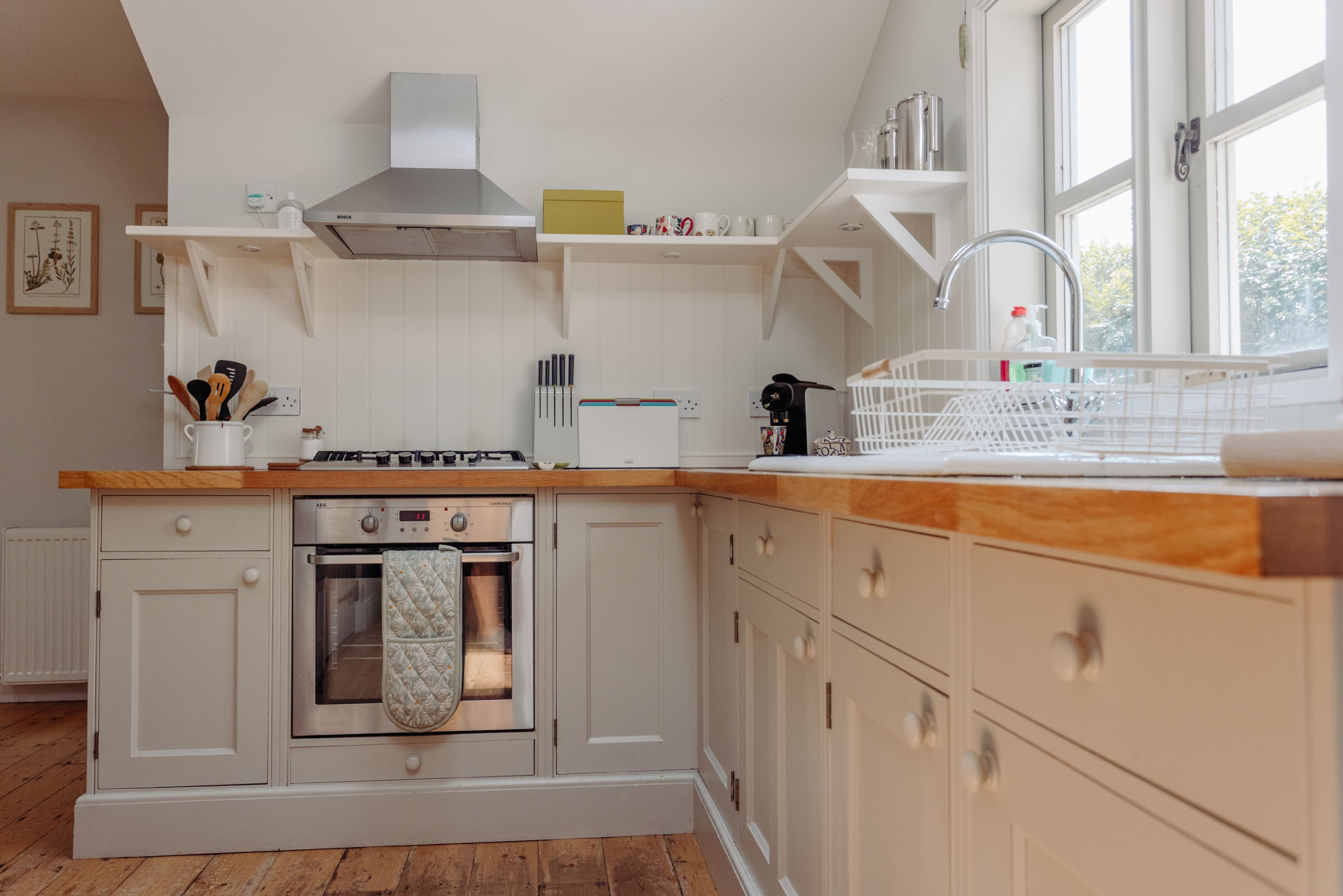 Een keuken met witte kasten, een houten aanrechtblad, een inbouwoven en een spoelbak.