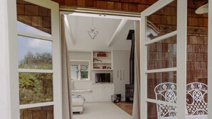 Un umbral abierto que da a una habitación con un sofá blanco, una pequeña cocina y una silla de metal blanca.