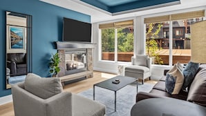 A modern living room with a fireplace, comfortable seating, and large windows offering a view of the outside.