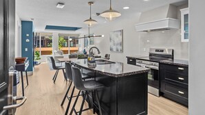 A modern kitchen with a central island, black bar stools, and pendant lighting.
